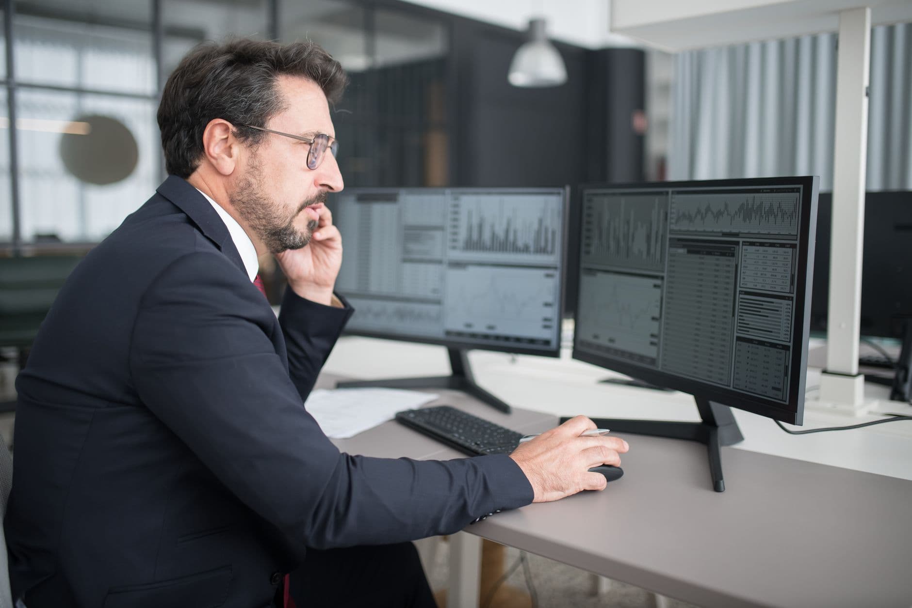 A freight broker's workspace with dual monitors showing shipment data and lane maps